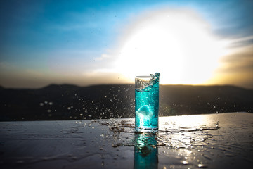 Cooling summer drink concept. Cocktail glasses splashing on sunset. Close up wet glass of cold...