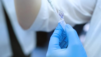 Close-up scientist selects a blue reagent from a small test tube using a thin pipette. - Powered by Adobe