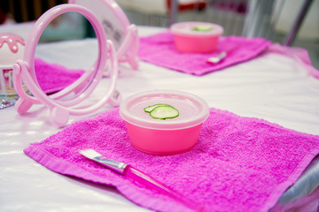Obraz na płótnie Canvas Children's game tool kit for girls home facial skin. Face mask with cucumber on a table.
