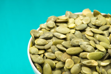 Pumpkin seeds in a bowl on turquoise background