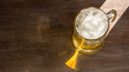 Mug of beer with a cap of foam, illuminated by the bright sun on a dark wooden background. Copy space, top view.
