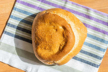 A loaf of homemade wheat bread on a rustic striped kitchen towel, top view, natural light