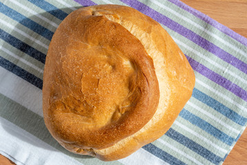 A loaf of homemade wheat bread on a rustic striped kitchen towel, top view, natural light