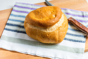 A loaf of homemade wheat bread on a rustic striped kitchen towel and a knife with a wooden handle, top view, natural light