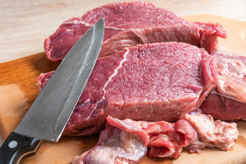 Cutting a piece of beef with a cook's knife on a cutting wooden board close-up