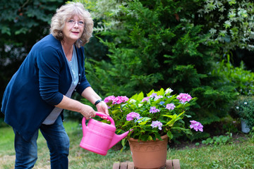Blonde Frau arbeitet im Garten mit Blumen und Gießkanne