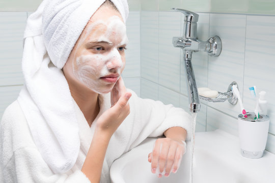 Girl In A White Robe Washes Her Face With Soap Suds In The Bathroom