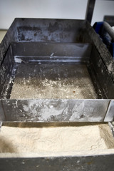 White filtered refined flour in a big restaurant industrial bakery stainless metallic container with a grid filter strainer. Unhealthy food. It can produce cancer and osteoporosis.