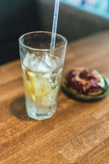 Cold lemonade with ice and lemons in a tall glass with a disposable tube. Chocolate donut with dressing.