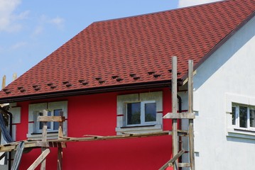 Naklejka premium part of an unfinished house with a red wall and windows under a brown tiled roof