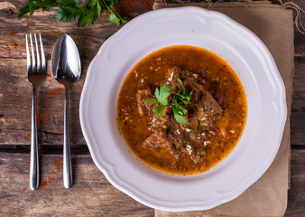 Beef with spicy sauce and parsley a white plate on rustic wooden table