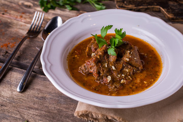 Beef with spicy sauce and parsley a white plate on rustic wooden table