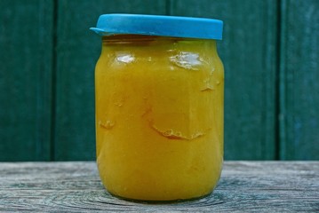 one closed glass jar of yellow honey stands on a gray table by the green wall