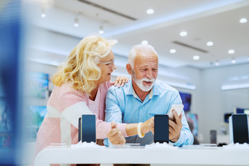 Cute smiling senior couple standing in tech store and choosing new smart phone.
