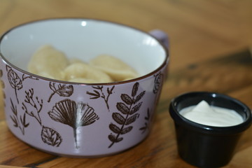  Dumplings of potatoes in enamelled pink dishes and sour cream on a wooden kitchen table