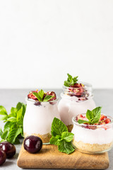 No baked cheesecake with cherry in glass jars, fresh cherries and mint on a grey stone background. Healthy dessert. Copy space.