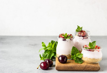 No baked cheesecake with cherry in glass jars, fresh cherries and mint on a grey stone background. Healthy dessert. Copy space.