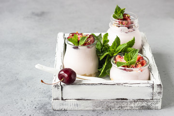 No baked cheesecake with cherry in glass jars, fresh cherries and mint on a grey stone background. Healthy dessert. Copy space.
