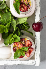 No baked cheesecake with cherry in glass jars, fresh cherries and mint on a grey stone background. Healthy dessert. Copy space.