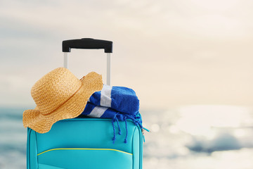 holidays. travel concept. blue suitcase with female hat and beach towel infront of tropical background