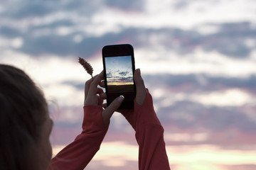 A girl photographs the sunset on a smartphone