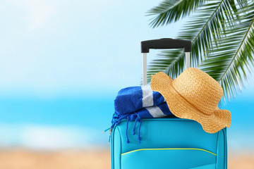 holidays. travel concept. blue suitcase with female hat and beach towel infront of tropical background