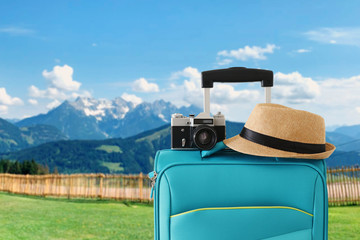 recreation image of traveler luggage, camera and fedora hat infront of a rural lanscape. holiday and vacation concept