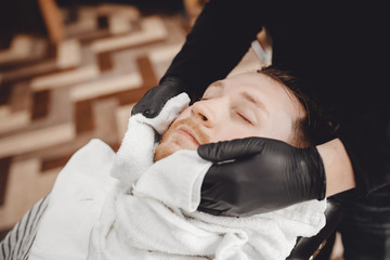 Man sits in barbershop chair and steam his face with hot towel in front of royal beard shaving razor