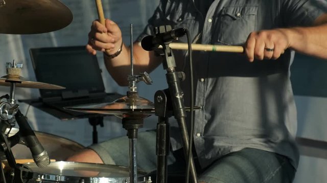 A young man plays the drum kit in the setting sun at a concert. close up.