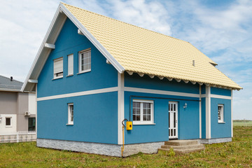 Fototapeta na wymiar a small blue house with white windows and a light yellow metal roof.