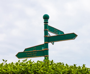 Green road sign on the crossroads with blue cloudy sky and green grass in the background.