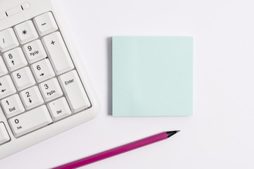 White pc keyboard with empty note paper and pencil above white background.