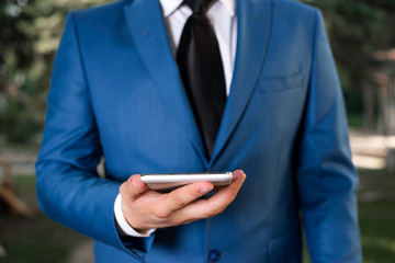 Businessman in blue suite stands with mobile phone in hands.