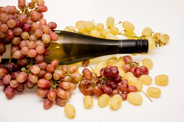 Red grapes, white grapes and a bottle of wine on neutral background