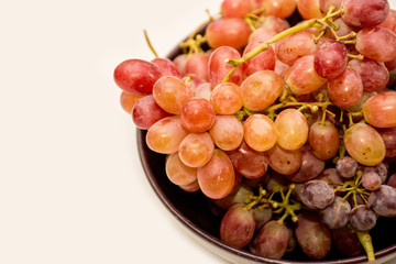 Bowl of red ripe grapes on neutral background