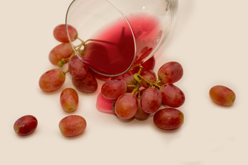 Red ripe juicy grapes, a wine glass and some spilled wine on neutral background. Splash of wine