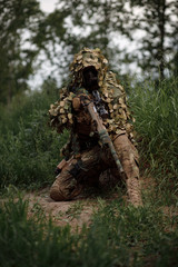 Airsoft soldier in full ammunition with rifle playing strikeball in outdoor in grass