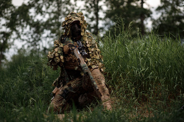 Airsoft soldier in full ammunition with rifle playing strikeball in outdoor in grass