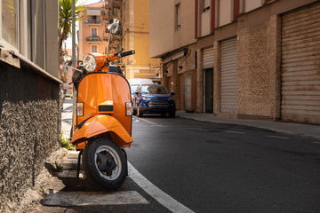 Plakat bright classic orange scooter with a round headlight parked on an Italian street