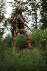 Airsoft soldier in full ammunition with rifle playing strikeball in outdoor in grass