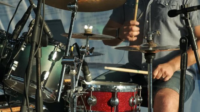 A young man plays the drum kit in the setting sun at a concert. close up.