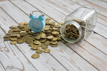 jar of coins with analog alarm clock on vintage wooden table.Financial and investment concept.