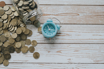 jar of coins with analog alarm clock on vintage wooden table.Financial and investment concept.