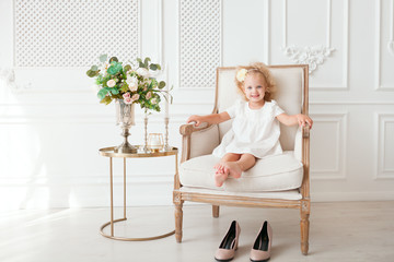 Little pretty girl in white dress trying on mummy's shoes