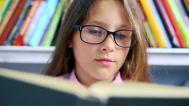 A little girl with glasses reads a book and turns over the pages reacting to what he saw.