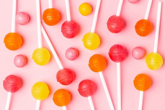 Pink, orange and yellow sweet candy lolipop on a pastel pink background