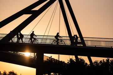 Düsseldorf 2019: Silhouette of Pedestrians and two persons riding a bike on bridge over the rhine in sunset