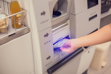 The child hand is picking up banknotes from the automatic payment machine. self service machine in modern supermarket, self-service pay point tills, self-checkout machine in hypermarket.