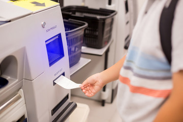 The child hand is picking up the receipt from the automatic payment machine. self service machine in modern supermarket, self-service pay point tills, self-checkout machine in hypermarket.