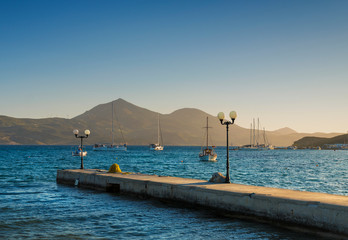 pier with street lighters in sun lights with view to bay and mountains on greek island Milos in Greece